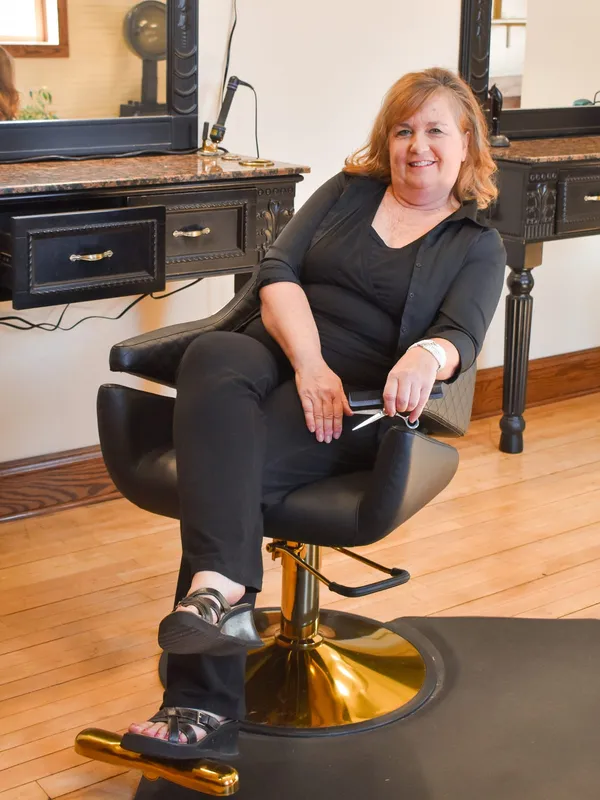 Laura Anderson seated in a styling chair at her station, holding scissors and a comb