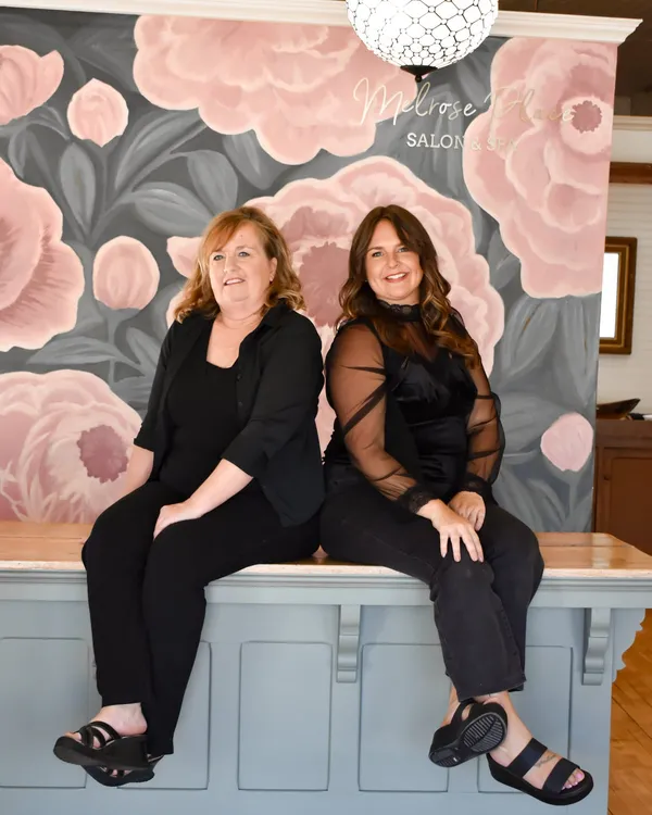 Two women seated side by side on the front desk, in front of the painted floral mural