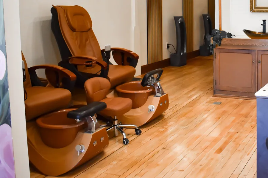 Pedicure area with tan leather pedicure chairs and foot basins on a wood floor