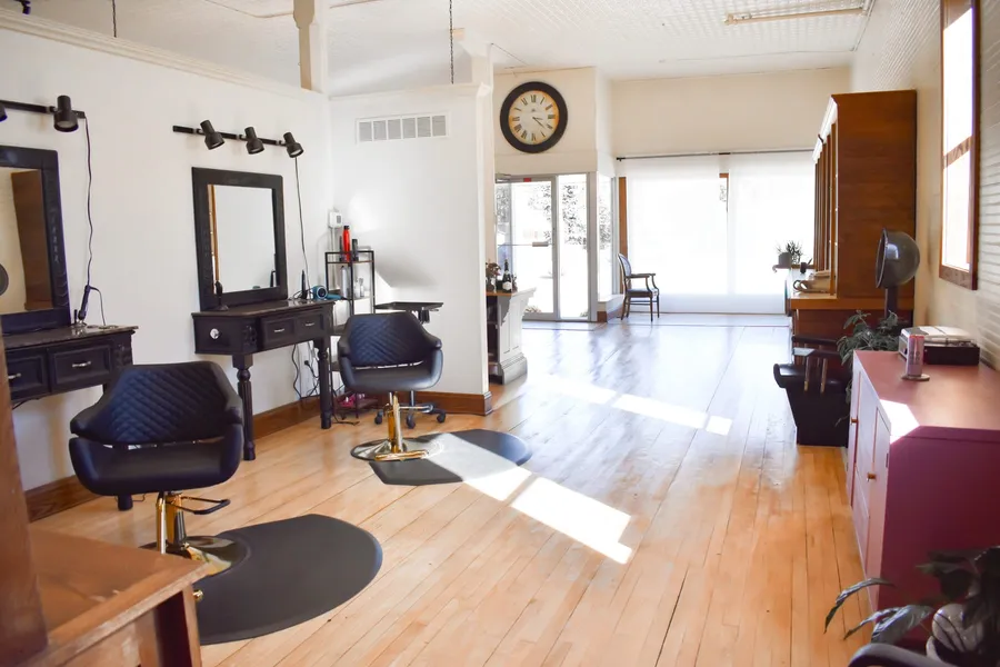 Salon floor with black styling chairs at mirrored stations, looking toward the front door and large windows